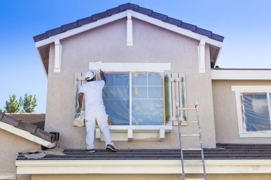 Painter painting exterior house trim above a window on a stucco home